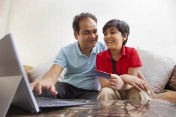 Father and son together shopping online through laptop using credit card