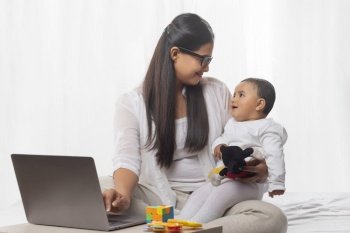 Mother holding her child while using laptop