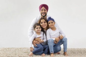 SIKH BOY AND GIRL SITTING ON MOTHER'S LAP AND FATHER HUGGING THEM