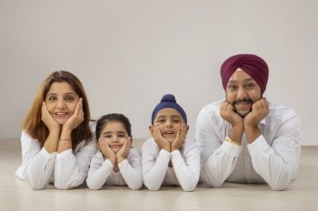 A HAPPY SIKH FAMILY SMILING AND POSING TOGETHER ON FLOOR WITH HANDS ON CHIN
