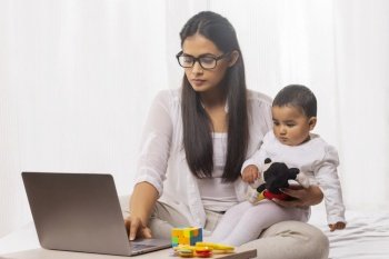 Mother holding child in her lap while using laptop