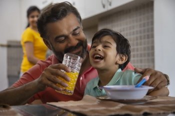 Close-up portrait of caring father feeding orange juice to his little child and mother standing behind