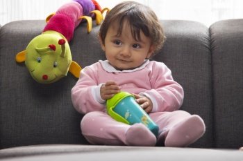 Cute baby leaning on sofa with water bottle and looking away