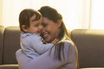 Mother hugging and caressing her baby in living room