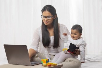Mother holding child in her lap while using laptop