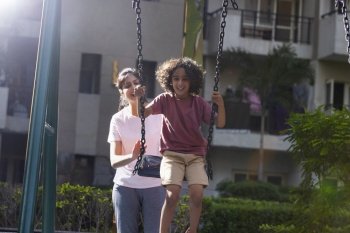 Mother pushing her son on swing in the park