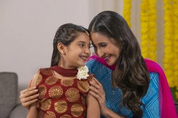 A mother adoring her daughter dressed in traditional wear with festive flower decoration behind.
