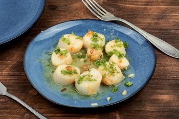 Roasted scallops with green on a plate, seafood. Delicatessen sea scallop. Wooden background.. Grilled scallop with butter sauce