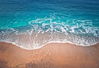 Blue ocean waves hits the shoreline. Beautiful texture of turquoise sea water and golden sandy beach. Tropical summer seaside background