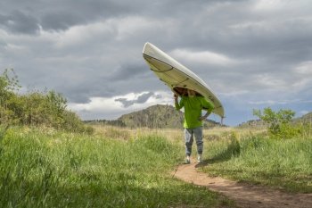 senior male is portaging a decked expedition canoe at foothills of northern Colorado in spring scenery