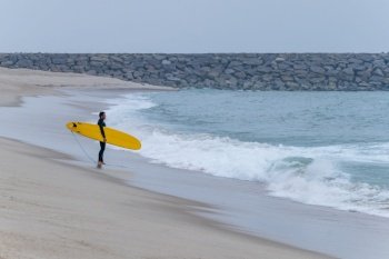 Surfer with board under his arm on a cloudy morning at Furadouro beach, Ovar - Portugal.