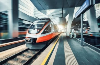 High speed train in motion inside modern train station in Vienna. Fast red intercity passenger train with motion blur effect. Railway platform. Railroad in Europe. Commercial transportation. Transport. High speed train in motion on the railway station at sunset