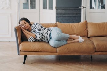 Overworked young african american woman is sleeping on leather couch at home. Leisure and recreation at home, weekend morning. Mixed race lady fell asleep in living room. Daytime nap on sofa.. Overworked young woman is sleeping on leather couch at home. Daytime nap on sofa.