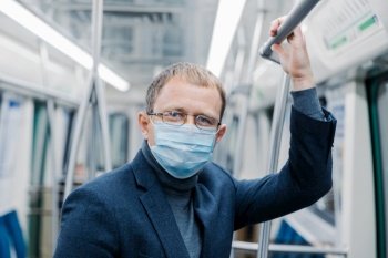 Coronavirus prevention. Man office worker wears transparent glasses, formal outfit, medical mask, ?ares about safety, poses in metro train, travels in public transport during Covid-19 outbreak.