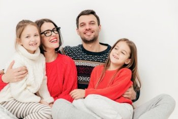 Family, children and people concept. Happy delighted cute mother, unshaven father and their children pose together against white background, spend free time at home. Family lifestyle concept.