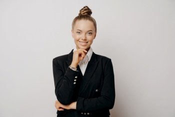 Portrait of joyful female office worker in casual clothes, confident body language with hand on her chin, business woman feeling happy and ready to work, looking forward alone against light wall. Happy female office worker with hand on chin