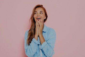 Excited woman with delightfully surprised look, touching both cheeks with hands, expresses positive emotions, wears casual blue shirt, happy to receive present or very good news. Body language. Close up shot of woman with delightfully surprised look