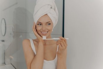 Attractive happy young girl with perfect white wide smile brushing her teeth in bathroom in front of camera after taking morning shower. Dental health and hygiene concept. Attractive happy young girl with perfect white wide smile brushing her teeth