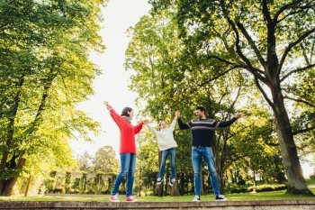 Handsome man wears sweater and jeans, beautiful woman in red knitted sweater and little adorable girl keeps with hands her parents, stand against beautiful nature background. Spending time together