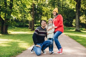 Carefree restful family have walk together, enjoy sunny autumn weather, green beautiful park and fresh air, pose into camera, embrace each other, have model relationship. Joyful child and parents