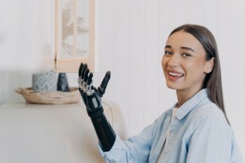 Pretty handicapped girl is opening cupboard at kitchen. Happy european woman with artificial arm at home. Functions of modern bionic prosthesis. Routine of disabled person concept.. Pretty handicapped girl is opening cupboard at kitchen. Happy european woman with bionic prosthesis.