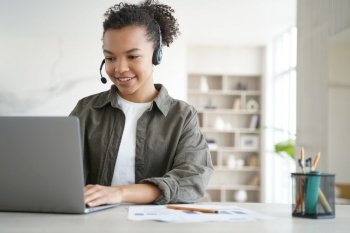 Smiling mixed race girl high school student in headset learning online at laptop at home. Modern biracial teen schoolgirl wearing headphones studying remotely. Distance education concept.. Mixed race girl high school student in headset learning online at laptop at home. Distance education
