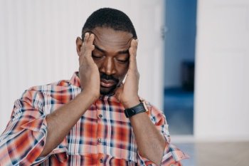 Exhausted upset african american man suffer from headache with his head in his hands. Tired overworked disappointed black guy suffering migraine. Stress at work, burnout, life crisis, failure.. Tired upset african american man suffer headache with his head in his hands. Stress at work, burnout