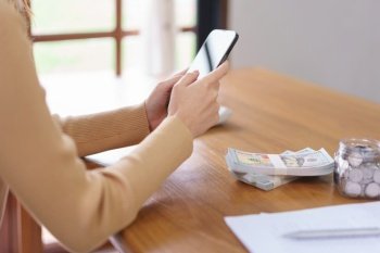 Saving money concept, Asian woman use smartphone and reading data after count the amount of savings.