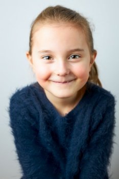 Portrait of adorable little girl. Cute small child looking at camera. Portrait of girl wearing blue sweater on white plain background