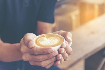 Close up man hands holding latte art coffee cup in cafe coffee shop. Hot coffee mug in man hands. Milk latte art fresh, relax in morning time