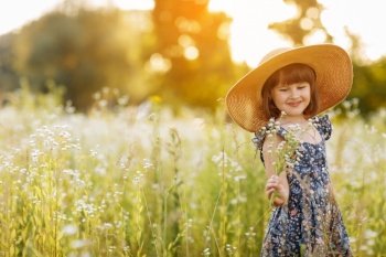 smiling child girl in a big mommys straw hat with bouquet of wildflowers in a green grassy meadow on summer sunny day. Happy childhood concept. Copy space. smiling child girl in a big mommys straw hat with bouquet of wildflowers in a green grassy meadow on summer sunny day. Happy childhood concept. Copy space.