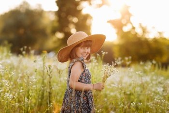 smiling child girl in a big mommys straw hat with bouquet of wildflowers in a green grassy meadow on summer sunny day. Happy childhood concept. Copy space. smiling child girl in a big mommys straw hat with bouquet of wildflowers in a green grassy meadow on summer sunny day. Happy childhood concept. Copy space.