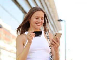 Happy smile young adult woman consumer using credit card and smartphone. people shopping via online application media concept. big shopping mall on summer day background with copy space.. Happy smile young adult woman consumer using credit card and smartphone. people shopping via online application media concept. big shopping mall on summer day background with copy space