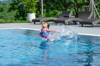 Little girl plays in the outdoor swimming pool of tropical resort during family summer vacation. Kids learning to swim. Healthy Summer Activities for Kids.