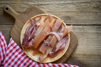 pickled squid on plate, raw squid for cooking food on wooden background, preserving food seafood - top view 