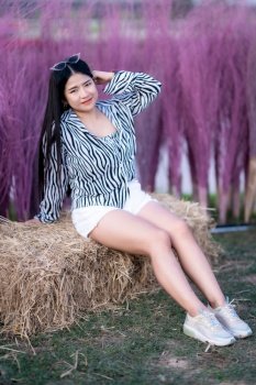 Portrait of asian Young woman happy traveler with black and white pattern dress enjoying sitting on the straw in and meadow grass purple color in the nature garden of in Thailand,travel relax vacation