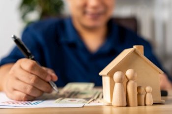 Selective focus for House model and figures people in front Happy Asian man holding a banknote and do financial accounting, Concept for financial planning, mortgage estate, Insurance, and home loan