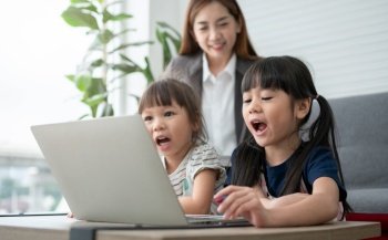 Asian mother with her two grandchildren having fun and playing education games online with a digital computer laptop at home in the living room. Concept of online education and caring from parents.