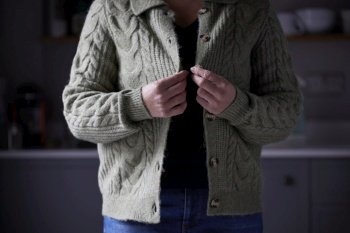 Woman Putting On Extra Jumper Clothing Trying To Keep Warm During Cost Of Living Energy Crisis