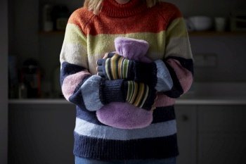 Woman In Gloves Hugging Hot Water Bottle Trying To Keep Warm During Cost Of Living Energy Crisis