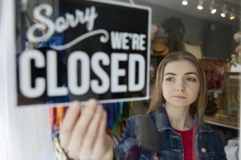 Sad Female Owner Of Small Business Turning Round Closed Sign In Shop Window
