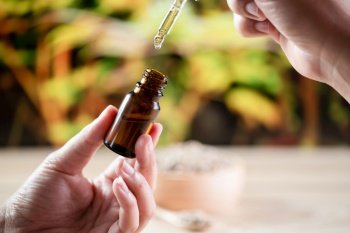 Hands holding a bottle of CBD oil and its dropper lid, with hemp leaf in the background. Legalized CBD product for medical purposes.. Hands holding a bottle of legalized CBD oil and its dropper lid with hemp leaf.