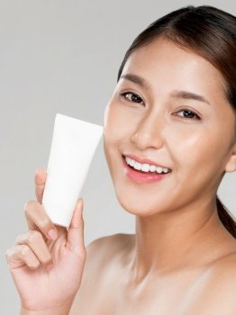 Ardent woman smiling holding mockup product for advertising text place, light grey background. Concept of healthcare for skin, beauty care product for advertising.. Ardent woman smiling holding mockup product for advertising text place.