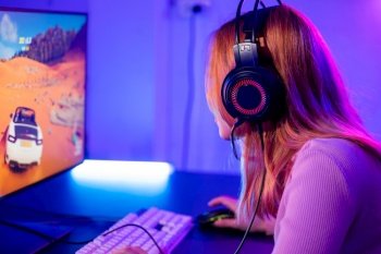 Young player woman wearing gaming headphones intend to do playing live stream games online at home, Happy Gamer endeavor plays online video games tournament with computer with neon lights, Back view