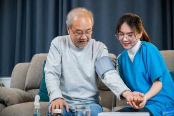 Asian doctor woman examine do checking old man client heart rate with pulsimeter monitor, nurse visit patient senior man at home she measuring arterial blood pressure on arm in living room, Healthcare