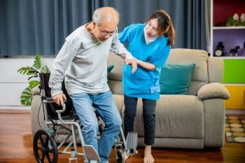 Doctor support old man to getting up to exercise, help handicapped elderly stand up, Asian woman nurse helping senior man patient get up from wheelchair for practice walking at home, physical therapy