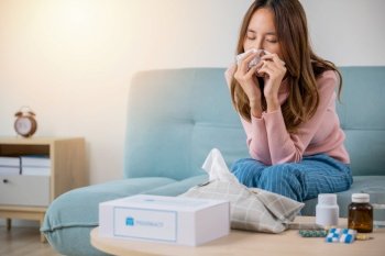 Sick woman. Asian young girl cold sick she sneeze with tissue paper on sofa, beautiful female health problem blowing nose use pharmacy kit box delivery service from hospital, delivery pharmacy concept