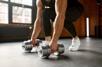 Strong man with athletic arms lifting dumbbells from gym club floor. Bodybuilding workout concept. Strong man lifting dumbbells from floor