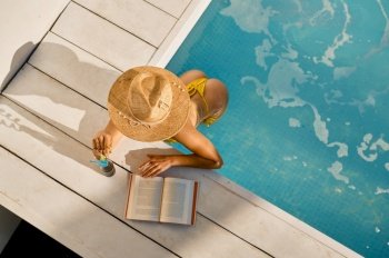 View from above on woman reading and drinking refreshing cocktail at swimming pool. Vacation and travel concept. View from above on woman reading and drinking at swimming pool