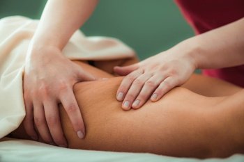 Relaxing legs massage, hands of a female massage therapist massaging female client’s legs